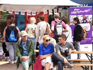 Einige Interessierte vor dem AWO-Stand. Ein Banner vom Büro Kinderarmut steht am Stand. Davor sitzen Menschen an Biertischgarnituren.