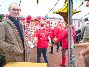 Ein Mann mit Brille stteht am linken Bildrand, dahinter eine Line Dance - Gruppe in roten T-Shirts und mit roten Weihnachtsmützen. Im weihnachtlichen Festzelt.