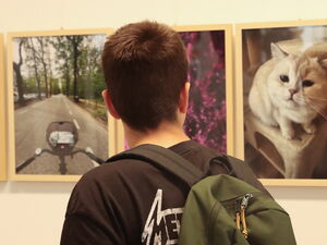 Fotoausstellung. Person mit Rucksack schaut sich gerahmte Fotografien an.