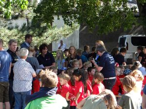 Draußen, Sonne scheint. Ca. 10 Kinder in roten T-Shirts umringt von anderen Kindern und Erwachsenen.