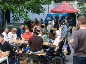 Festszene draußen. Menschen sitzen fröhlich an Tischen zusammen.