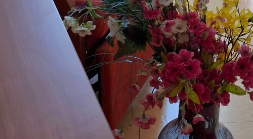 Blumenvase mit unechten Blumen steht auf dem Boden.