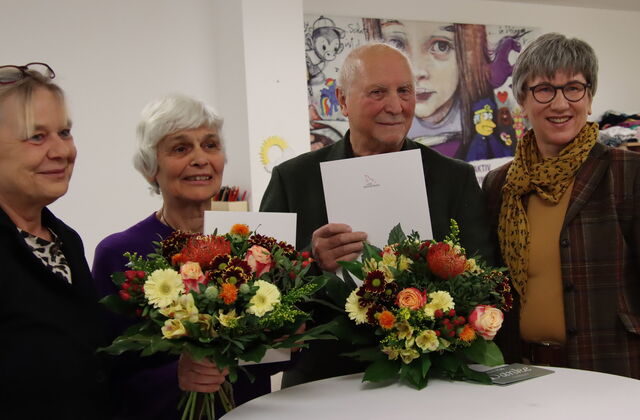 4 Personen stehen um einen Stehtisch. Ältere Frau und älterer Mann sind in der Mitte und halten Freude strahlend ihre Blumen in der Hand. Festlicher Anlass.