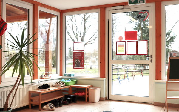 Verglaster Eingangsbereich mit kleinem Schuhregal in er Ecke. Blick nach draußen.