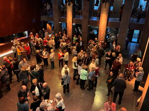 Foyer von oben. Menschen stehen in kleinen Gruppen, trinken, unterhalten sich.