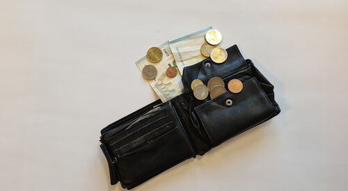 Eine geöffnete schwarze Geldbörse liegt auf einer hellen Fläche, darin und daneben liegen mehrere Euro-Münzen.