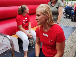 Neben der Hüpfburg. Zwei Frauen in roten AWO T-Shirts sitzen bei der roten Hüpfburg, sie machen eine Pause.