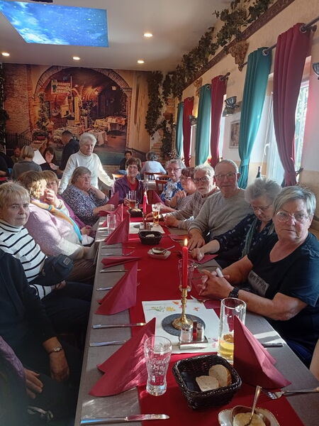 Restaurant. Langer gedeckter Tisch mit rotem Läufer und Kerzen. Menschen sitzen am Tisch.