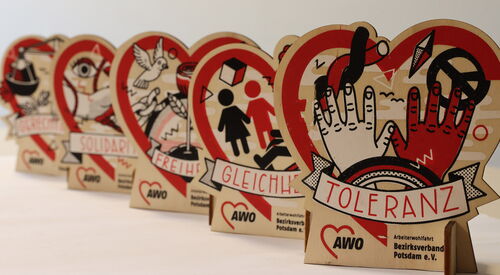 Tischaufsteller. In Herzform. Hintereinander aufgereiht. Beschriftet mit: Toleranz, Gleichheit, Freiheit, Solidarität. Bemalt mit Händen, Peace-Logo, weiße Taube