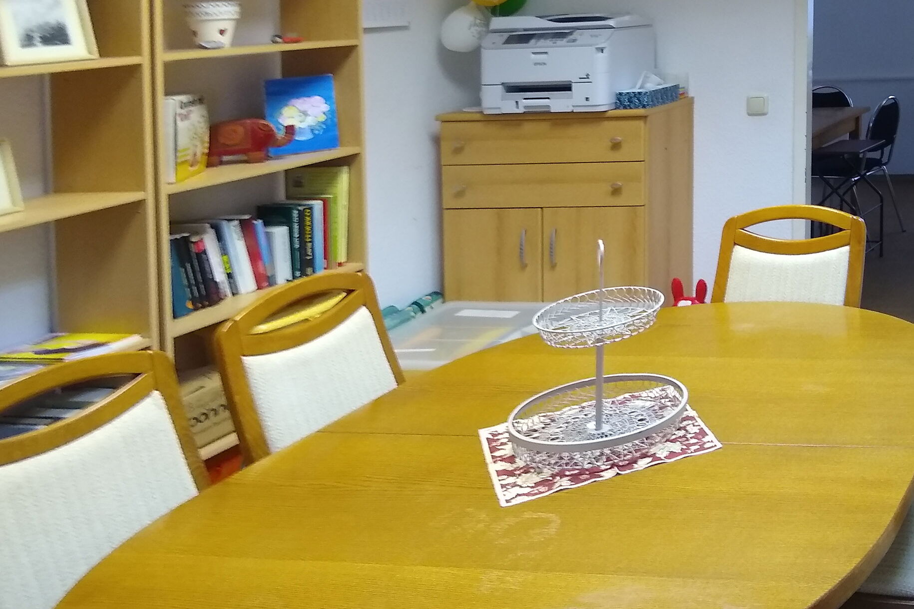 heller Raum mit einem großen, ovalen Holztisch im Mittelpunkt. 6 gepolsterte Stühle stehen am Tisch.