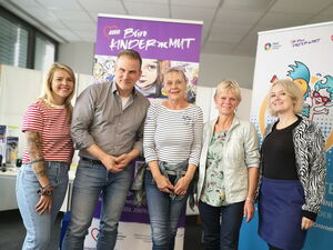 Gruppenbild vor dem lila Roll up Banner vom Büro Kinder(ar)mut. 4 Frauen, ein Mann. Alle lächeln fröhlich in die Kamera.
