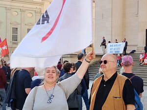 Menschen auf dem AltenMarkt bei einer Demo. Im Vordergrund eine Person die eine weiße AWO Fahne schwenkt, daneben ein Mann mit Sonnenbrille.