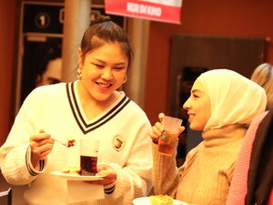 Zwei Frauen stehen im Kino Foyer mit Kuchen und Getränk, bei lächeln. Lockere Atmosphäre.