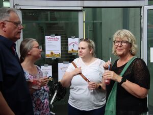 Vor einem Eingang zum Gebäude an dessen Tür info-Zettel kleben, stehen 3 Frauen und ein Mann, jeder hat einen AWO Becher mit Getränk in der Hand.