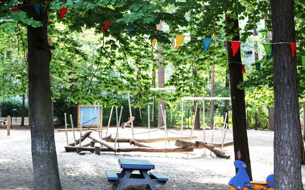 Spielplatz zwischen Bäumen. Gerüst zum Balancieren aus Holzstämmen, Schaukeln, Wippe.