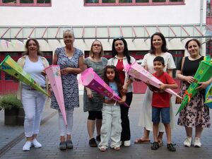 Draußen vor einem Gebäude. 6 Frauen, ein Mädchen und ein Junge. Sie halten leere Zuckertüten in den Händen. Sie lächeln fröhlich.