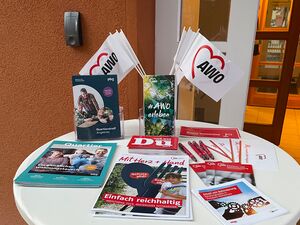 Ein weißer Stehtisch vor einem Gebäude mit Info-Material der  AWO.
