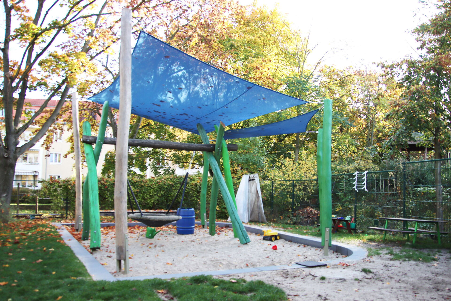 Spielplatz, großer Sandkasten mit Affenschaukel und einer blauen Plane als Überdachung.