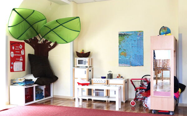 Kinderküche mit Herd, Spüle und Mikrowelle. Rechts daneben ein Puppen Kinderwagen und eine Garderobe.