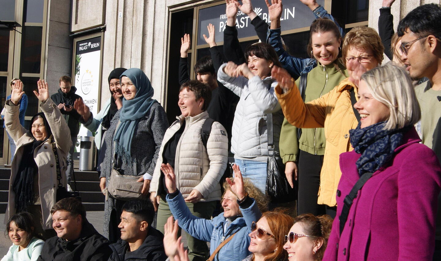 Vor dem Friedrichstadt-Palast Berlin stehen Menschen, einige winken mit beiden Händen über dem Kopf. Fröhliche Gruppe.