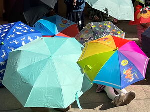 Bei Sonne. Viele Kinder sitzen und stehen auf einem Weg, von vielen bunten Regenschirmen verdeckt.