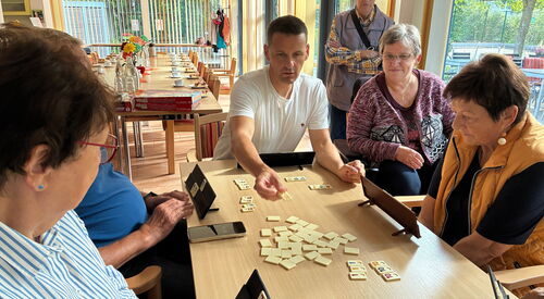 Ein Mann im weißen T-Shirt legt ein Plättchen mit Zahl an. Spiele Runde.