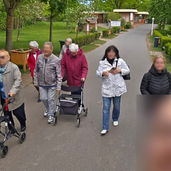 Kleine Gruppe geht einen Weg entlang. Zwei Menschen gehen am Rollator.