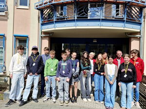 Gruppenbild vor dem Eingang eines Gebäudes. 15 Personen. 4 Erwachsene in roten AWO Jacken und Schüler.