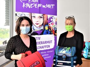 Im Büro Kinderarmut: Zwei Frauen mit Mund-Nasen-Schutz Masken. Jede hat einen Schulranzen in den Händen. Baerbock hat einen roten Ranzen, Schweers einen blauen Ranzen.