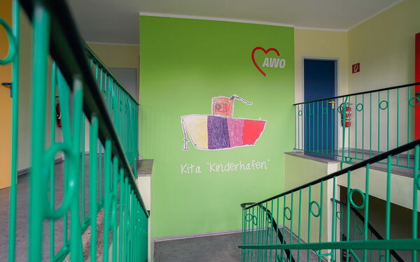 Treppenhaus in Grün. Auf einer Wand das AWO Logo und ein buntes Schiff mit Anker. Unter dem Schiff steht in weißer Schrift Kita "Kinderhafen".