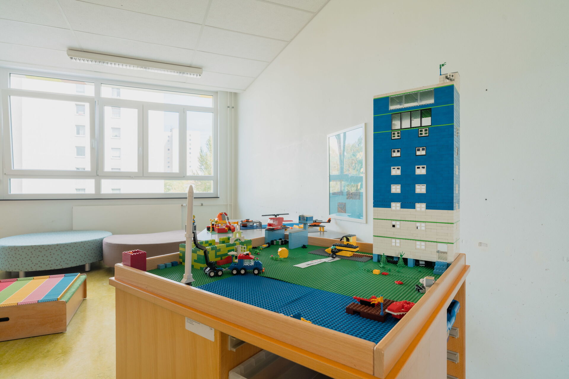 Spielzimmer. Lego Tisch, bebaut mit einem Hochhaus vor dem Bäume stehen, Hubschrauber und ein Baufahrzeug sind auf dem Tisch verteilt.