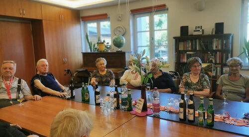 Alte Frauen und Männer an einem großen Tisch. Auf dem Tisch stehen Getränke und Gläser.