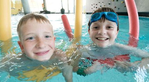 2 fröhliche Kinder beim schwimmen im Hallenbad.
