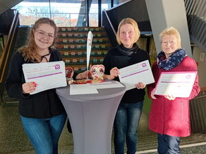 Stehtisch in der Schule, 3 Frauen stehen rechts und links daneben und halten die Unterschriftenlisten in die Kamera.