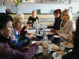 6 Frauen am Tisch bei Kaffee und kuchen. An den Wänden schwarz-weiß Fotografien.