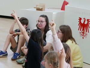 Kinder sitzen auf dem Fußboden im Plenarsaal. Einige melden sich.