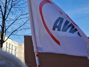 Eine weiße Fahne mit AWO Logo weht im Wind. Blauer Himmel, Sonnenschein.