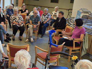 Großer Raum, Kantine, viele Menschen sitzen kreisförmig. Diskussionsrunde.