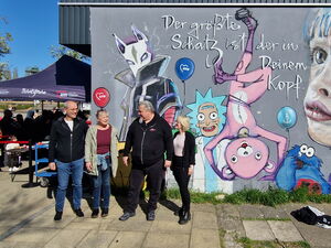 Gruppenbild. 4 Personen, 2 Männer, 2 Frauen vor eine bunten mit Figuren bemalten Graffiti Wand.