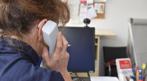 Frau von hinten an einem Schreibtisch sitzend mit Telefonhörer am Ohr.