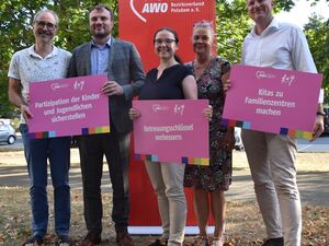 Portrait: 5 Menschen stehen vor einem roten AWO Roll-Up-Banner. Alle lächeln in die Kamera. Sie stehen draußen, die Sonne scheint.
