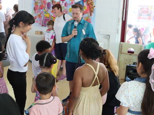 Aaron Langner, Leiter des AWO Eltern-Kind-Zentrums, spricht in ein Mikrofon und wird dabei von Kindern umschart.