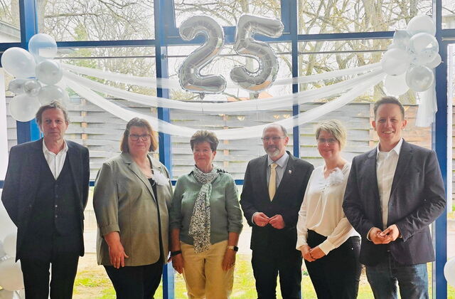 Gruppenbild mit Bürgermeister. 3 Frauen, 3 Männer vor einer Glaswand. Blick nach draußen. Über Ihnen hängt eine silberne Luftballon-25 und weiße Luftballons links und rechts..
