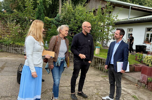 2 Frauen und 2 Männer draußen. Rechts im Hintergrund ein weißes Haus.