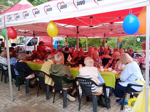 Pavillons mit Luftballons geschmückt. Menschen sitzen bei Kaffee und Kuchen darunter an langen Tischen.