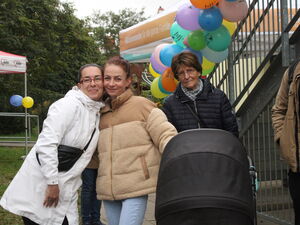 3 Frauen, die in die Kamera lächeln. Die Frau rechts etwas älter hat einen Kinderwagen vor sich.