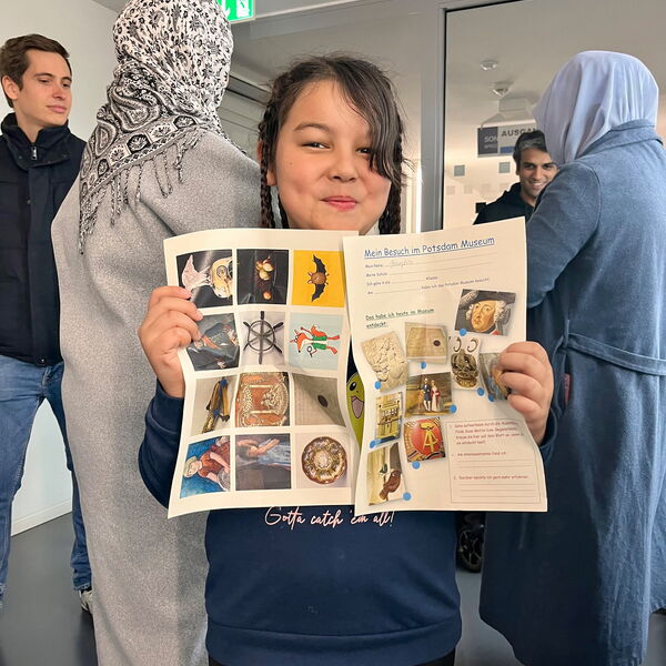 Mädchen hält zwei A4 Seiten in die Kamera. Ein Quiz vom Potsdam Museum.