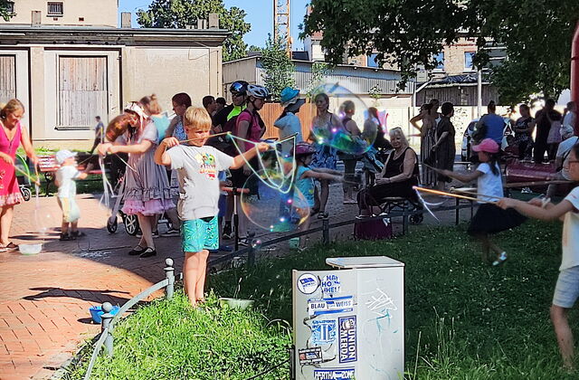 Draußen bei warmen Wetter, Sonne scheint. Kinder und Erwachsene machen Riesen-Seifenblasen.