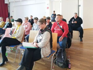 Teilnehmende sitzen in Stuhlreihen in einem großen Raum.