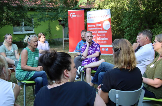 Menschen die in zwei Stuhlkreisen sitzen und miteinander ins Gespräch kommen. Im Hintergrund zwei große AWO Roll-Up Banner